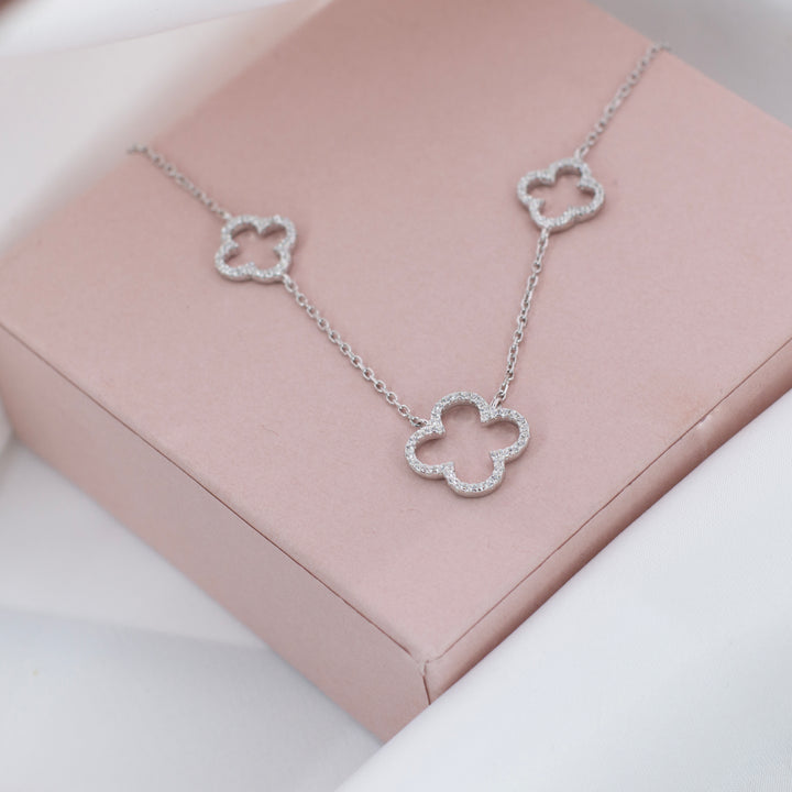 Silver necklace with two small and one large four leaf clovers with sparkling gemstones in. Placed on top of a jewellery gift box.