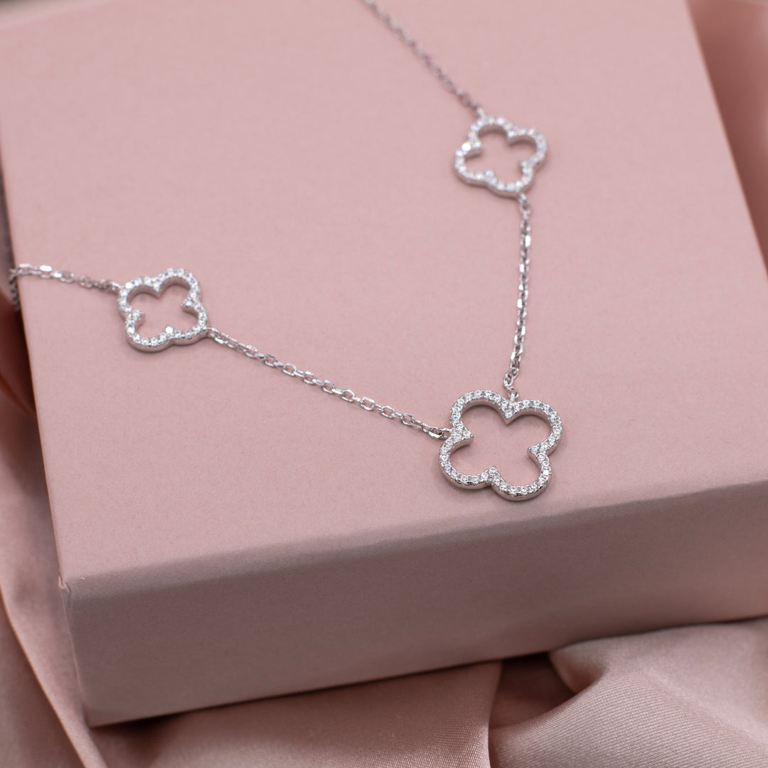 Silver necklace with two small and one large four leaf clovers with sparkling gemstones in. Placed on top of a jewellery gift box.
