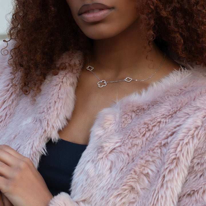 Woman wearing pink fluffy jacket and silver four leaf clover necklace.