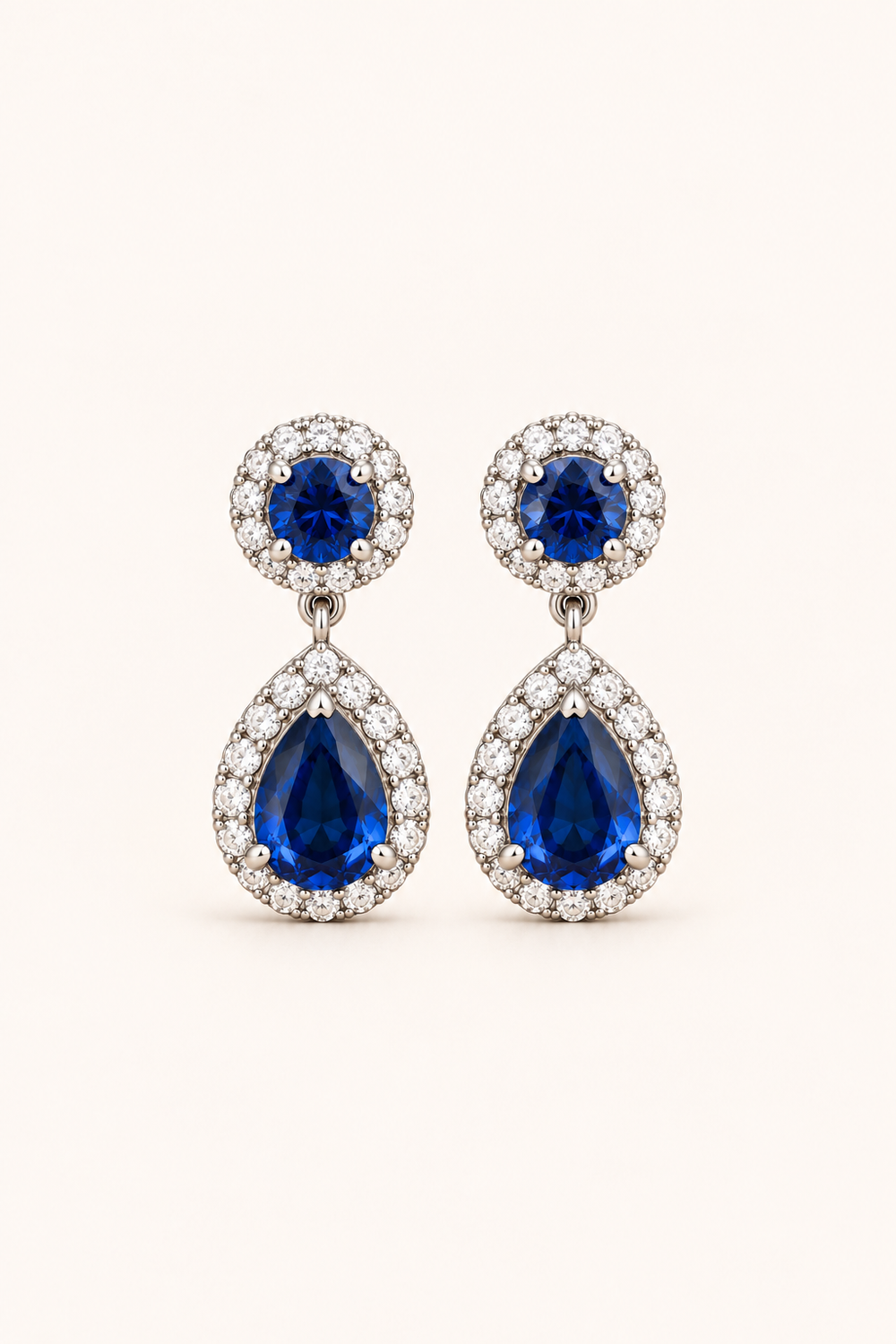 Blue halo pear drop earrings in 9ct white gold on a plain cream background