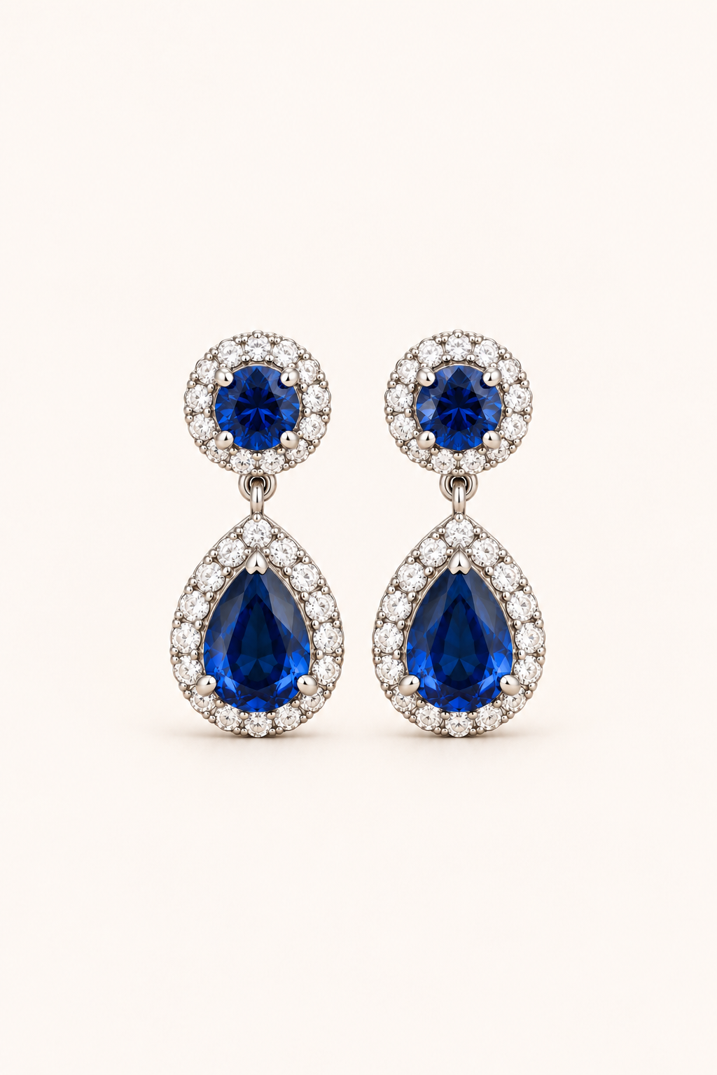 Blue halo pear drop earrings in 9ct white gold on a plain cream background
