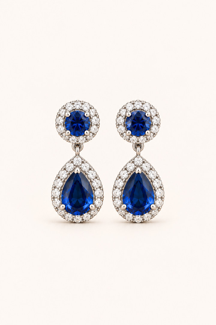 Blue halo pear drop earrings in 9ct white gold on a plain cream background
